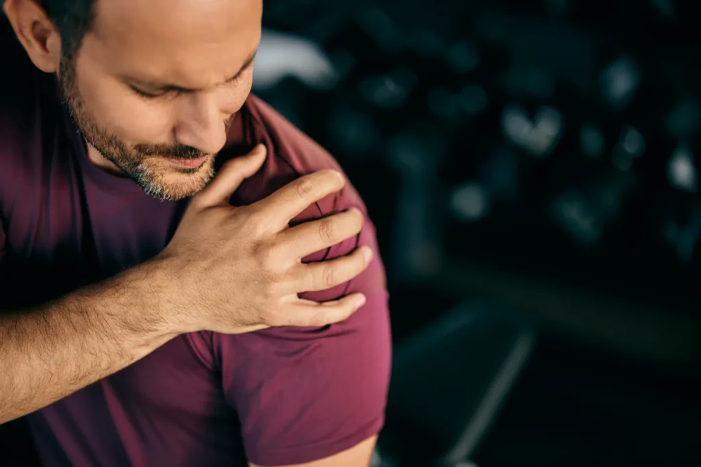 Someone holding a shoulder in pain who needs a shoulder arthroscopy surgery.