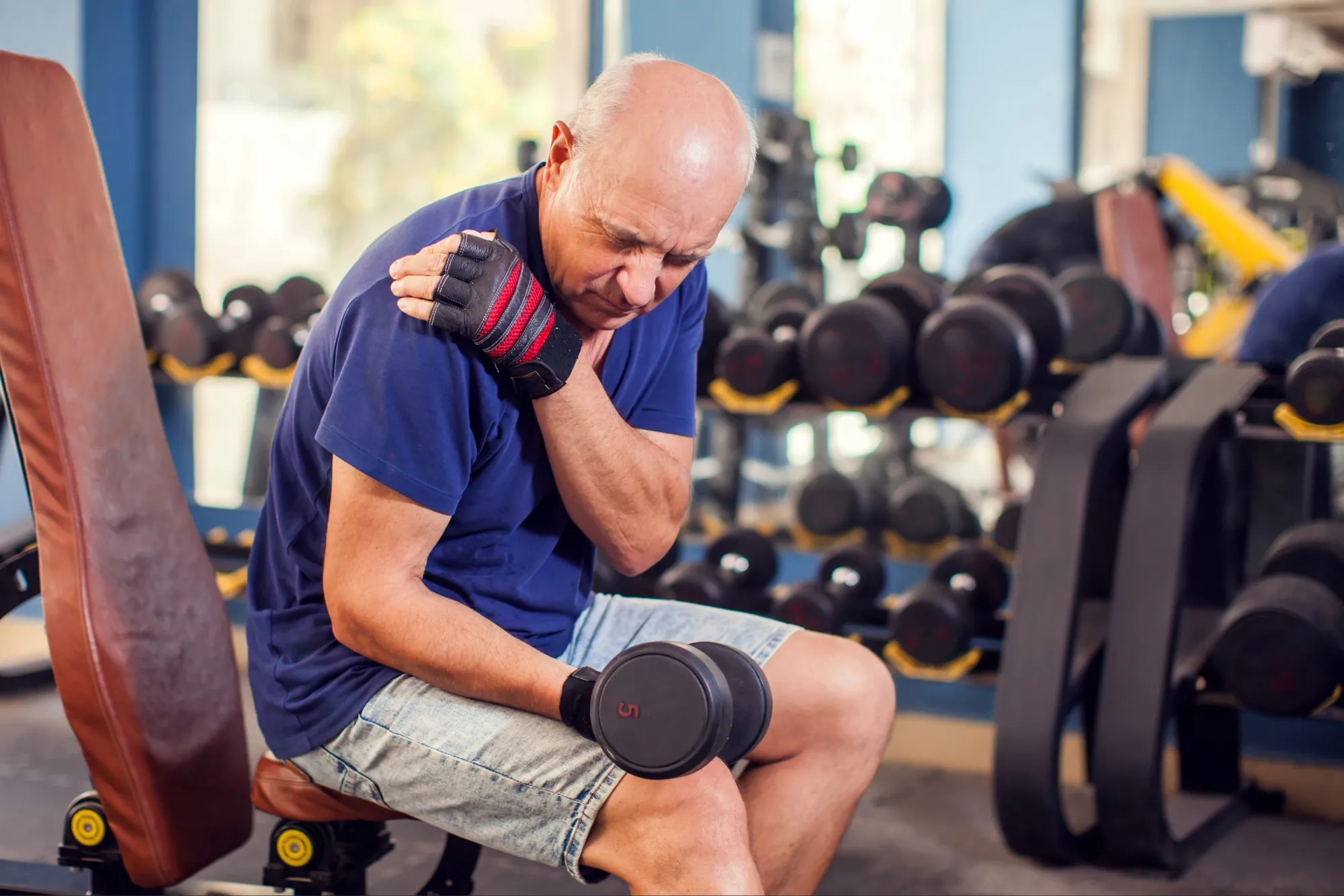 Older man holding his sore shoulder while lifting a dumbbell at the gym